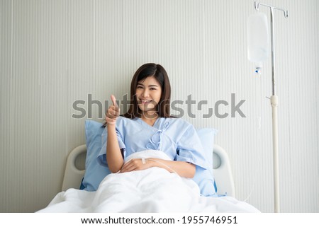 Happy Asian female patient smiling, lies on the bed, and raises thumb up to show confidence in treatment. Concept of believe in treatment And insurance coverage Royalty-Free Stock Photo #1955746951