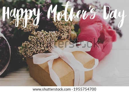 Happy mother's day greeting card. Happy mother's day text and gift box, peony, lilac and roses flowers on white wood. Stylish floral greetings. Handwritten lettering. Mothers day