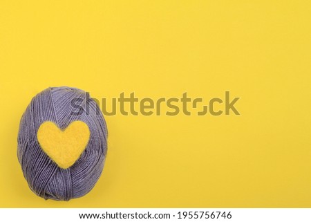 A yellow wool heart rests on a gray ball of knitting thread.The concept of handwork, needlework and needlework.The colors of 2021 are gray and yellow. Top view.Flat styling style