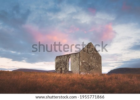 Old, ancient stone ruins of the remote and isolated Kilmuir Church in the Scottish rural countryside under a vibrant, colourful sunset or sunrise sky on the Isle of Skye, Scotland. Royalty-Free Stock Photo #1955771866