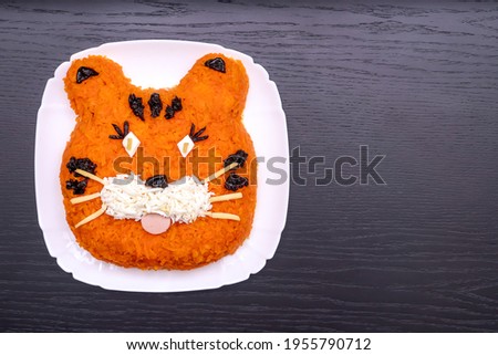 Funny salad in the form of the symbol of the tiger of 2022, made of carrots, eggs, cucumbers, potatoes, prunes, sausage. New Year's Christmas food top view copy space. Holiday, art of food