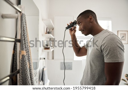 Young African man cutting his hair in his bathroom Royalty-Free Stock Photo #1955799418