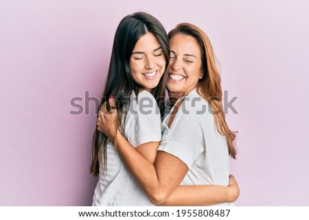 Beautiful hispanic mother and daughter smiling happy hugging over isolated pink background. Royalty-Free Stock Photo #1955808487