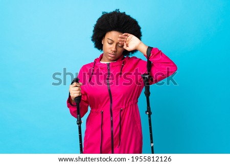 Young Africa American with backpack and trekking poles isolated on blue background with tired and sick expression