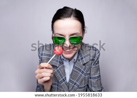 woman maneger in suit in a cage and green glasses eating a lollipop