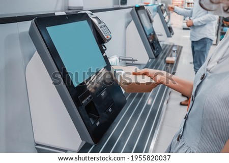 Woman scans barcode of her lunch box for cashless payment at the self-service checkout in the supermarket. Such machines kiosks allows to increase throughput and reduce queue in the store Royalty-Free Stock Photo #1955820037