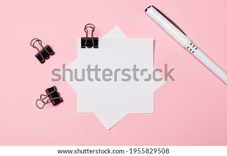 On a light pink background, black paper clips, a white pen and white note paper. Flat lay with copy space