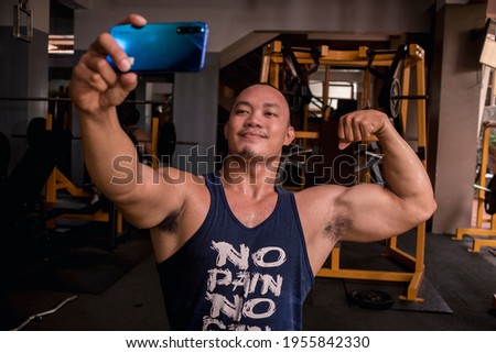 A large and brawny asian man takes a selfie of him doing a double bicep pose. Monitoring muscle gains or posting to social media.