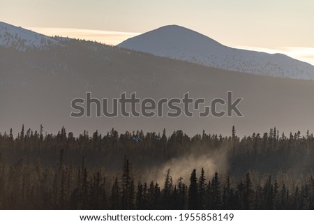 A hazy mountain view of wilderness area in northern Canada during the start of spring with wood smoke pouring out of the spruce, boreal forest below. 