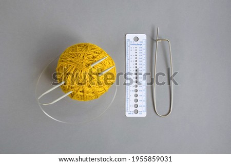 One skein of yellow wool yarn, knitting spokes, measuring ruler and large pin on gray background, handmade, knitting. Close-up. Copy space. Selective focus. Royalty-Free Stock Photo #1955859031