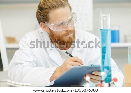 handsome young male scientist wearing protective glasses holding his clipboard