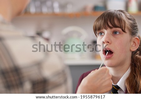 Mother Carrying Out Rapid Lateral Flow Test For Covid-19 On Daughter Wearing School Uniform At Home Royalty-Free Stock Photo #1955879617