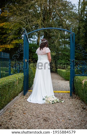 Picture of the elegant bride wearing cream long dress, standing back in the garden