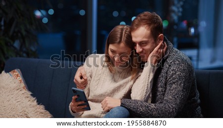 Young beautiful caucasian couple staying home using smartphone social media interacting taking photo selfie family picture in stylish apartment.