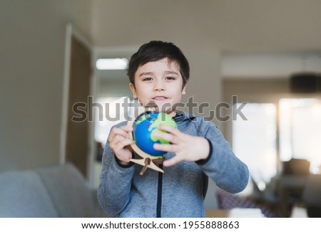 Portrait Kid is looking at a globe, School boy learning about Geography, young boy with happy face holding world map standing in living room, World Children s Day, Education and Homeschooling concept