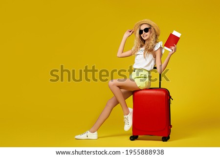 girl in hat with passport and ticket sitting on red suitcase