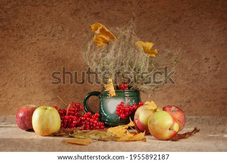 fresh apples, red viburnum, yellow maple leaves in a green vase on a brown background