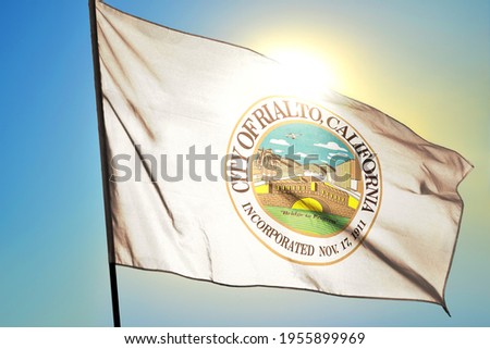 Rialto of California of United States flag waving on the wind in front of sun