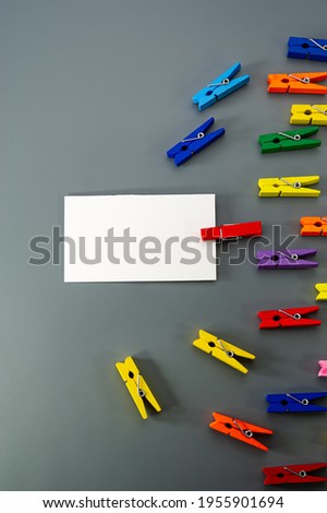 White rectangular paper and multicolored wooden clothespins lie on a gray background. Business concept. Cover.