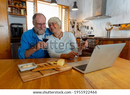 COVID-19 Stay connected and hope concept. Happy senior couple with wine video calling friends on laptop or online chatting with family celebrating easing of coronavirus restrictions and lockdown.