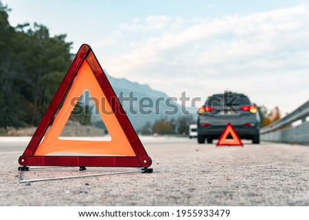 The warning triangle is at the back of the car at a safe distance.Car on the road behind warning triangle.The triangle placed behind the car.