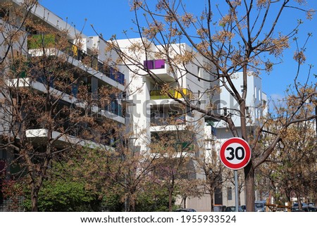 a French traffic sign for a speed limit of 30 in front of new residential buildings