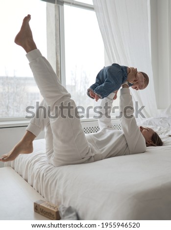 Home portrait of a baby boy with mother on the bed. Mom holding and kissing her child. Mother's day concept. High quality photo