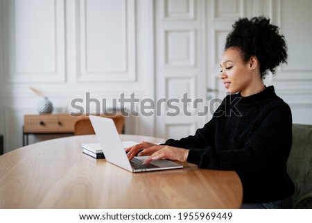 In the browser, working on a new work project. The freelancer works remotely on a laptop. A satisfied female designer smiles at an Afro-ethnic appearance. Curly black hair.