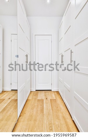 Perspective view of empty narrow hallway with white walls and wardrobe with mirror and parquet floor in minimalist style apartment