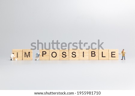 Miniature  people worker team on impossible word in wooden alphabet letters with prefix un crossed out, leaving the word possible Royalty-Free Stock Photo #1955981710