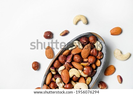 Different types of nuts in a ceramic snack plate and scattered on isolated white background. Nutrient dense vegan snacks. Clean eating concept. Close up, copy space for text, top view, flat lay. Royalty-Free Stock Photo #1956076294
