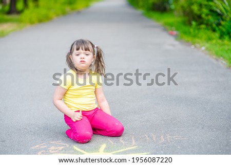 Young girl with syndrome down draws the sun with chalk on the asphalt 