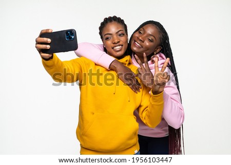 Two african women taking selfie photos with her cell phone on white background