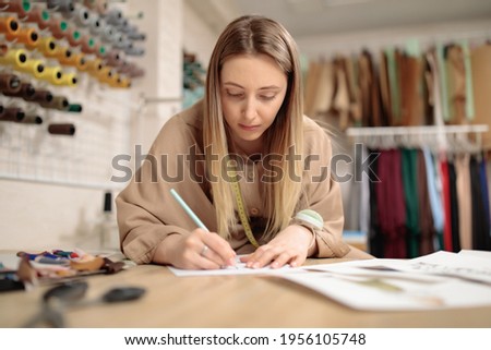 Young female artist fashion designer is drawing sketch at table in modern studio atelier. Small tailor business