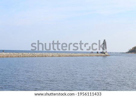 Beautiful view on summer lake. Calm water with small waves. Stones and reeds on the lake shore. Lighthouse on the lake. Warm summer weather in Karelia. Reflection on the water under sunshine.