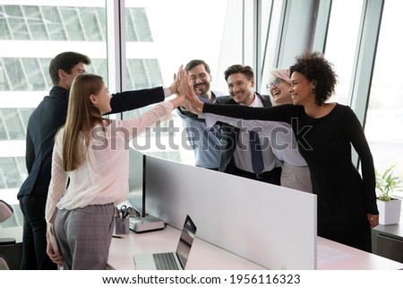 Excited multiethnic employees colleagues give high five celebrate shared work success or achievement. Overjoyed diverse multiracial businesspeople triumph engaged in teambuilding activity in office. Royalty-Free Stock Photo #1956116323