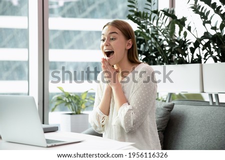 Overjoyed young female employee or worker look at computer screen surprised by good business news online. Happy excited Caucasian businesswoman triumph read about financial success on laptop. Royalty-Free Stock Photo #1956116326