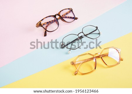 multiple eyeglasses on a multicolored background of pastel colors, geometric background, pink yellow and light blue colors, trendy eyeglass frames copy space Royalty-Free Stock Photo #1956123466