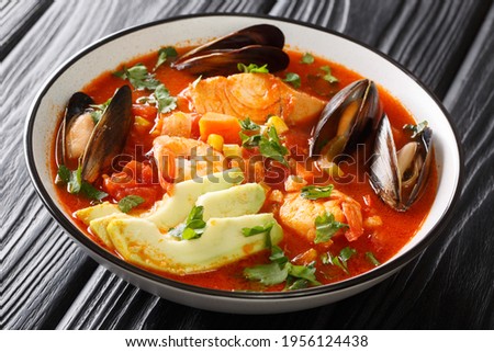 Sopa de Mariscos seafood soup with cod, shrimp, mussels, vegetables and avocado close-up in a bowl on the table. Horizontal

