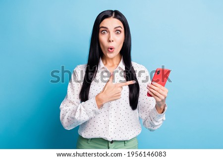 Photo of shocked brunette woman point finger phone wear white dotted shirt isolated on blue color background