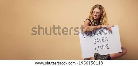 Woman holding a banner of "vaccination saves lives" slogan. Female sitting on brown background with lots of copy space.