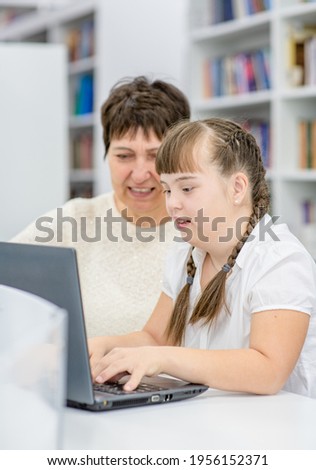 Young girl with down syndrome  uses a laptop with her teacher at library. Education for disabled children concept