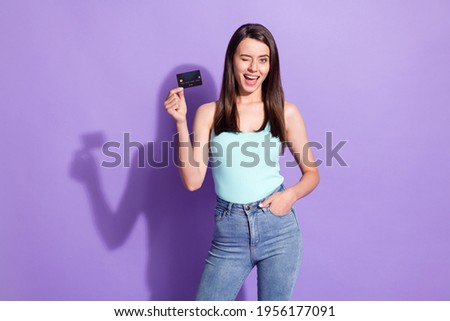 Photo of charming funky young woman wink eye hold credit card hand pocket isolated on purple color background