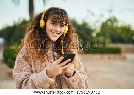 Young hispanic woman smiling happy using smartphone and headphones at the city