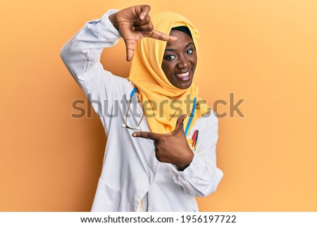 Beautiful african young woman wearing doctor uniform and hijab smiling making frame with hands and fingers with happy face. creativity and photography concept. 