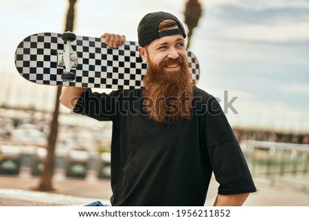 Young irish skater man smiling happy holding skate at the city.