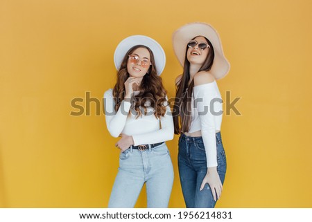 Picture of Two shocked girls pointing and looking away over yellow background