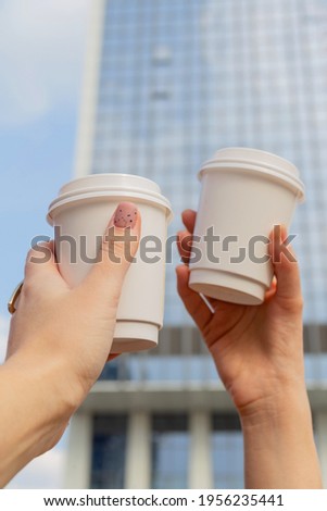 Two white cups with coffee to go in female hands against the background of city buildings and the sky. High quality photo