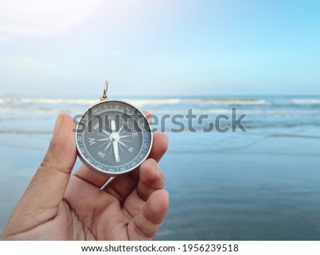 close up hand holding compass with blue sky and sea wallpaper background, travel bubble and relaxation, planning and manage to success business concept