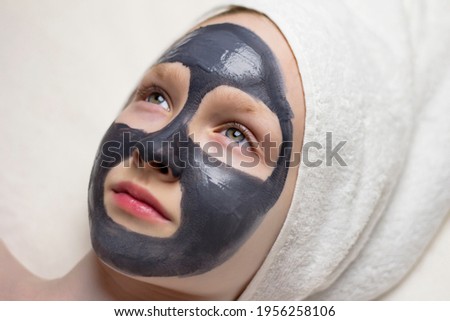 Girl's face with a purifying charcoal mask on a white background.